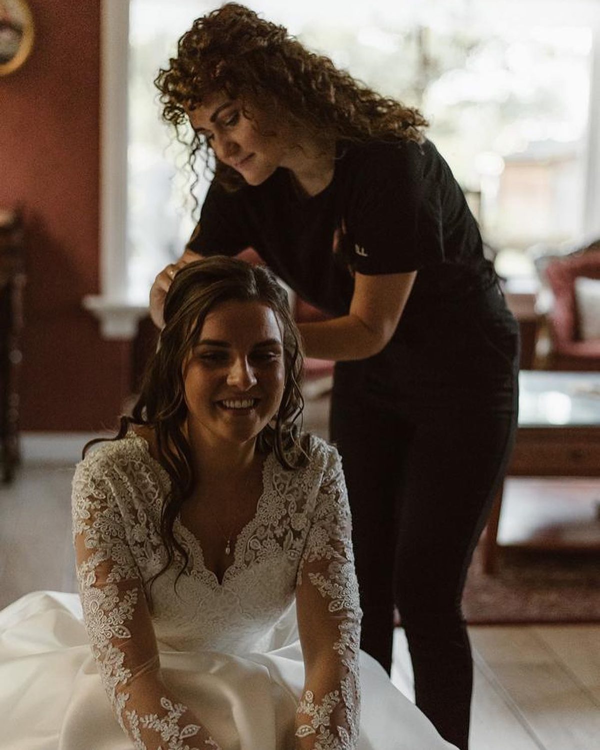 Een bruid in een kanten jurk krijgt haar haar opgestoken in de salon